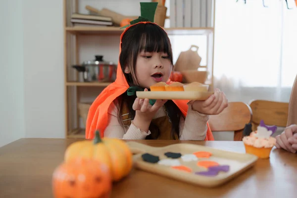 ハロウィンの若い女の子と母親がテーブルの上でお菓子やカップケーキを作っています ハッピーハロウィーンの日 — ストック写真