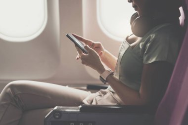 Neşeli Asyalı kadın uçakta oturur ve seyahat ederken cep telefonu kullanır..