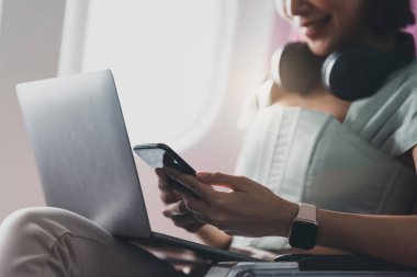 Neşeli Asyalı kadın seyahat ederken uçakta cep telefonu kullanıyor..
