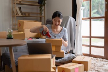 Asyalı küçük işletme sahibi ev ofisinde çalışıyor. Ticari perakende pazarı ve çevrimiçi pazarlama dağıtımı, KOBİ e-ticaret kavramı.