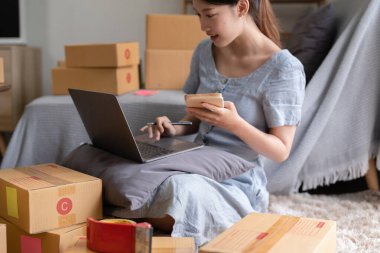Asyalı küçük işletme sahibi ev ofisinde çalışıyor. Ticari perakende pazarı ve çevrimiçi pazarlama dağıtımı, KOBİ e-ticaret kavramı.
