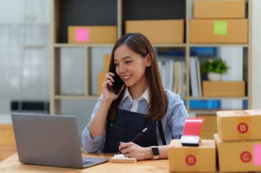 Asyalı küçük işletme sahibi ev ofisinde çalışıyor. Ticari perakende pazarı ve çevrimiçi pazarlama dağıtımı, KOBİ e-ticaret kavramı.