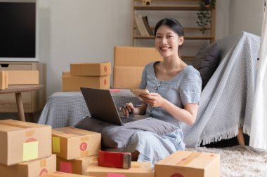 Asyalı küçük işletme sahibi ev ofisinde çalışıyor. Ticari perakende pazarı ve çevrimiçi pazarlama dağıtımı, KOBİ e-ticaret kavramı.