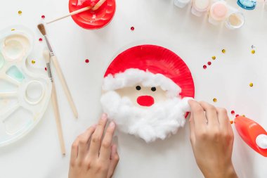 Çocuk, Noel Baba 'nın kağıt tabaktan yaptığı parçaları yapıştırıyor. El yapımı. Çocukların yaratıcılığı projesi, el işleri, çocuklar için el sanatları. DIY. Adım adım.