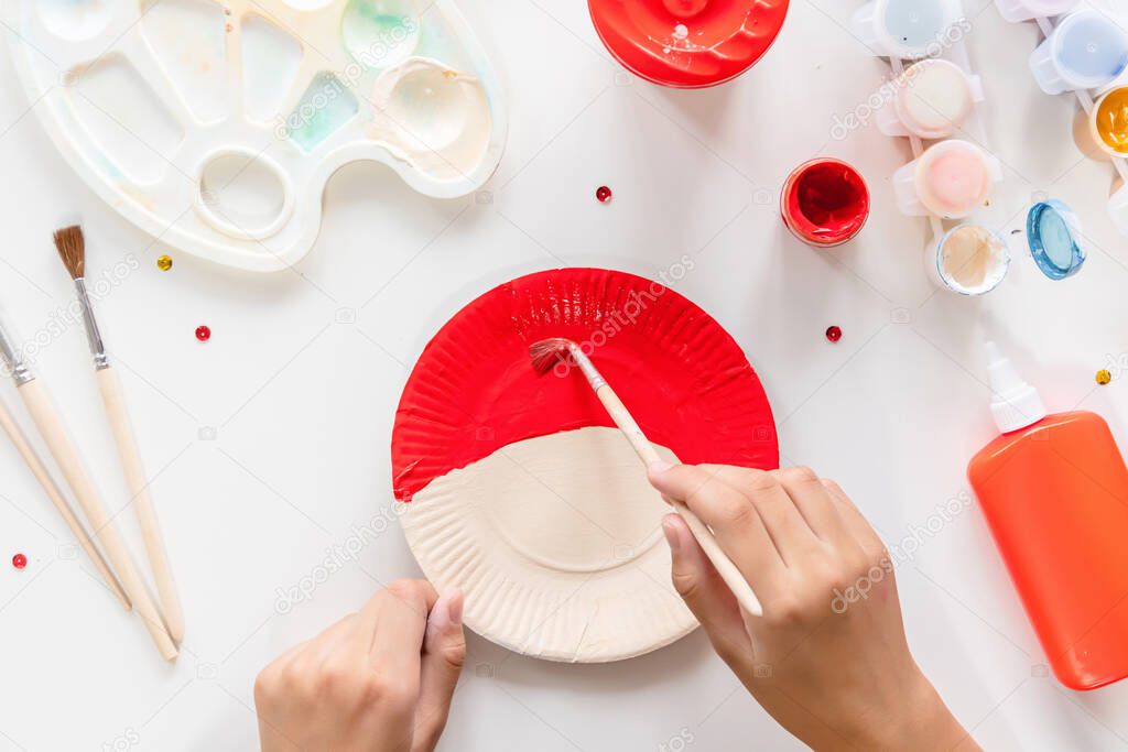 The child glues the parts Santa made from paper plate. Handmade. Project of children's creativity, handicrafts, crafts for kids. DIY. Step by step