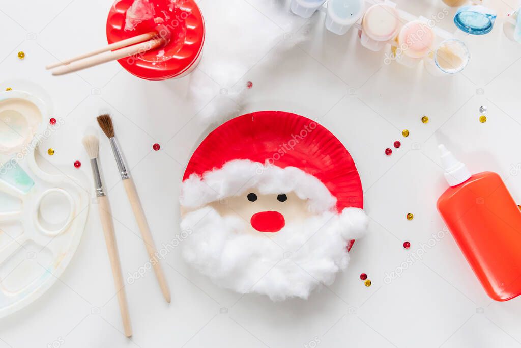 The child glues the parts Santa made from paper plate. Handmade. Project of children's creativity, handicrafts, crafts for kids. DIY. Step by step