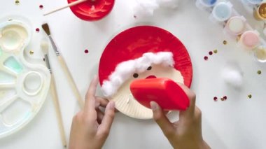 Çocuk, Noel Baba 'nın kağıt tabaktan yaptığı parçaları yapıştırıyor. El yapımı. Çocukların yaratıcılığı, el sanatları, çocuklar için el sanatları projesi.