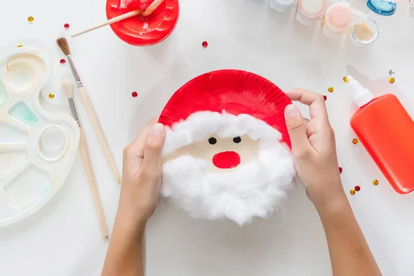 Çocuk, Noel Baba 'nın kağıt tabaktan yaptığı parçaları yapıştırıyor. El yapımı. Çocukların yaratıcılığı projesi, el işleri, çocuklar için el sanatları. DIY. Adım adım.