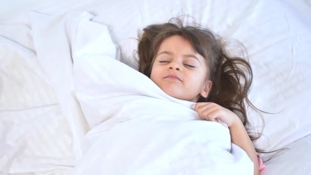 Imádnivaló sötét hajú lány alszik édesen reggel wihte ágynemű otthon. Gyermeki álmok, kényelem, nyugalom és béke. 4-5 éves lány. — Stock videók