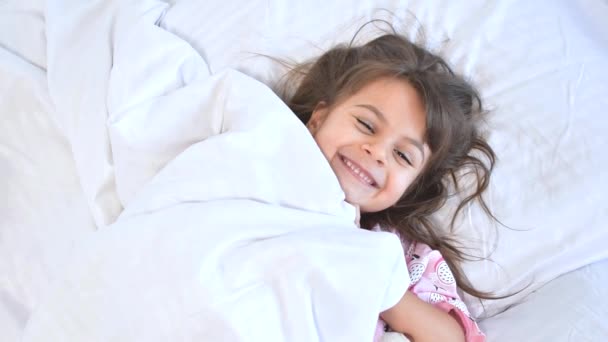 Αξιολάτρευτο μελαχρινό κορίτσι που κοιμάται γλυκά το πρωί πάνω σε σεντόνια στο σπίτι. Παιδικά όνειρα, άνεση, ξεκούραση και ειρήνη. — Αρχείο Βίντεο