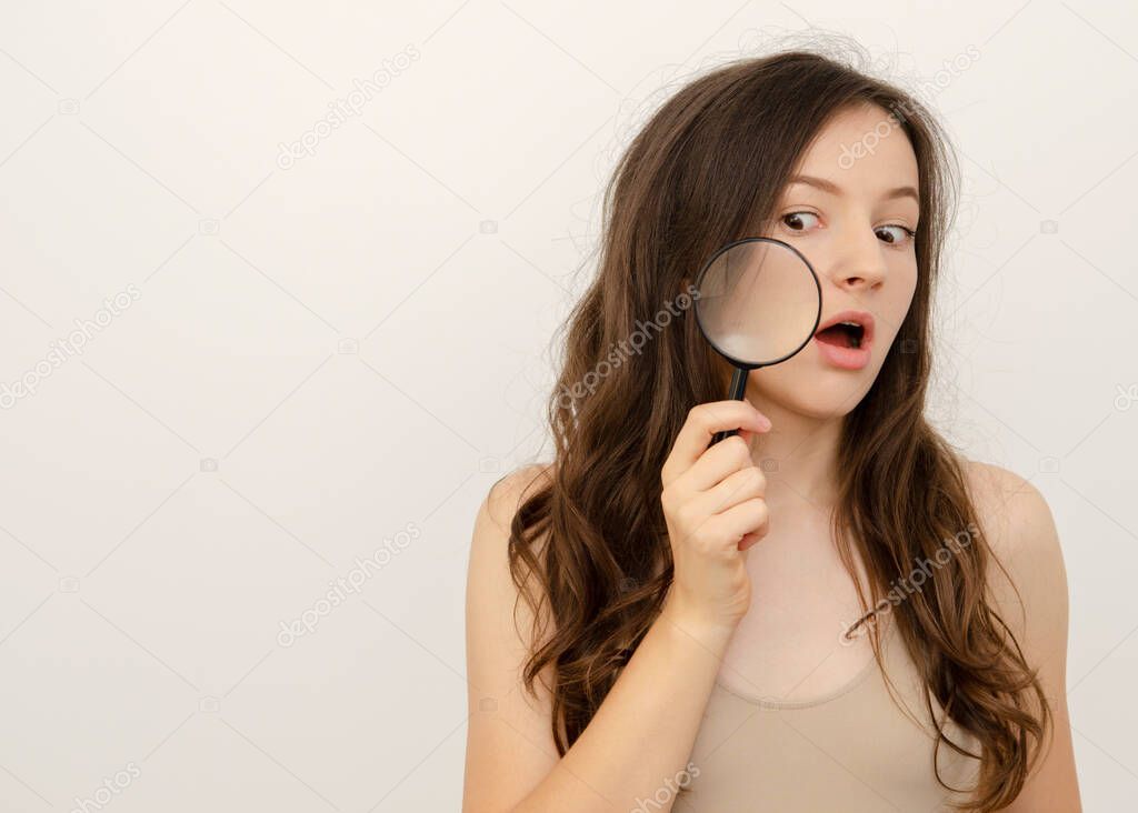 young beautiful woman holds a magnifying glass near her face skin