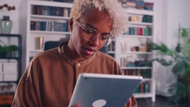 Çekici Afrikalı Amerikalı kadın sıcak bir odada otururken elinde tablet tutuyor.