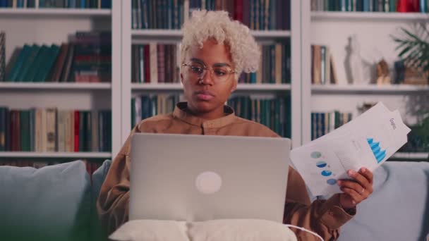 African American female with laptop looking documents with financial report — Stock Video