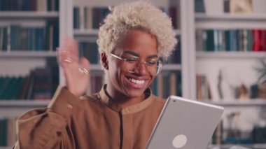 Afro-Amerikalı kadın kanepede oturup tablet üzerindeki video konferans uygulaması ile konuşuyor.
