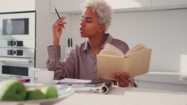 Ciddi odaklı Afro-Amerikan kadın ders kitabı okuyor, kalem tutuyor not alıyor.