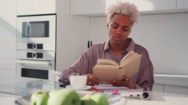 Afro-Amerikalı kadın elinde açık bir kitapla mutfağa bakmak istiyor.