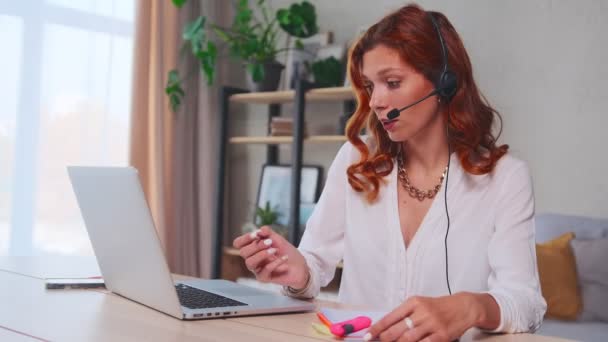 Caucásica mujer distante trabajador lleva auriculares videollamadas hace notas — Vídeos de Stock