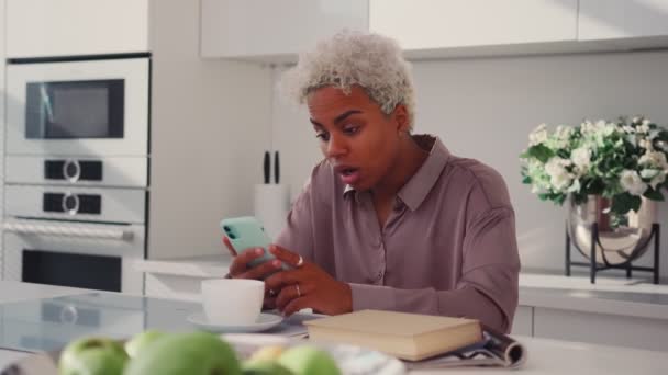 Zaniepokojona Latynoska kobieta ma problemy z telefonem komórkowym siedząc w kuchni — Wideo stockowe