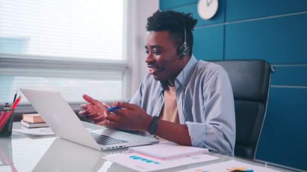 Selbstbewusster afrikanischer Geschäftsmann trägt Kopfhörer bei Konferenzschaltung am Laptop — Stockvideo