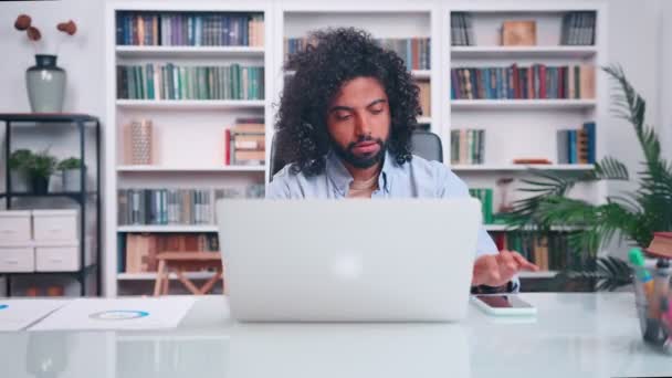 De jonge Arabische man die met laptop werkt neemt telefoon op en maakt bange blik. — Stockvideo