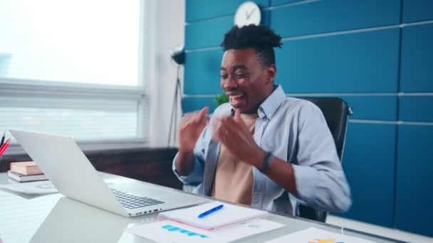 Joven hombre afroamericano se regocija por lo que vio en el ordenador portátil, risas y olas manos. — Vídeos de Stock