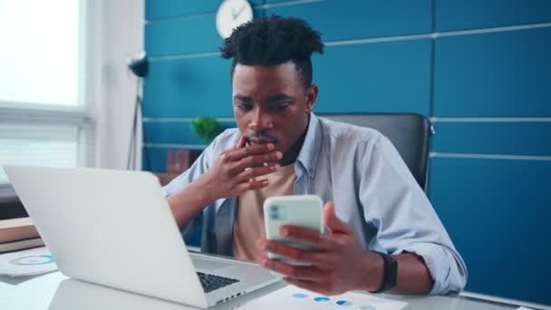 Hombre afroamericano se pone nervioso escribiendo datos de teléfono a portátil. — Vídeos de Stock