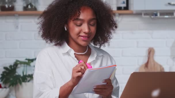 Framgångsrik afroamerikansk kvinna anteckna i anteckningsboken medan du tittar i laptop — Stockvideo