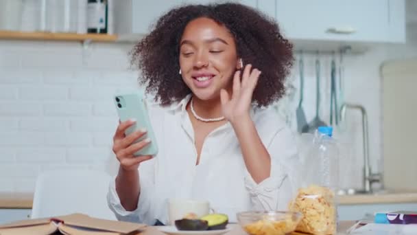 Feliz jovem afro-americano mulher acenando mão cumprimentando farands senta-se na cozinha — Vídeo de Stock