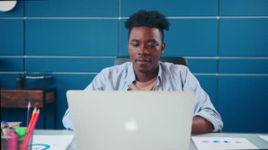 Başarılı Afrikalı Amerikalı adam dizüstü bilgisayarda yazı yazıp koltuğa mutlu bir şekilde oturuyor..