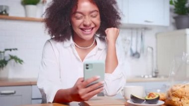 Başarılı genç Afrikalı Amerikalı kadın telefondaki video görüşmesi sırasında seviniyor.