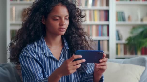 Indiai tizenéves lány kezében telefon, miközben nézi a képernyőn, miközben otthon ül. — Stock videók