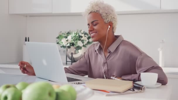 Vidám afro-amerikai nő nevet ül konyhaasztal laptoppal. — Stock videók