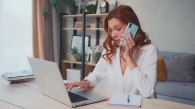 Başarılı beyaz kadın bilgisayarda çalışıyor ve aynı zamanda telefonla konuşuyor..