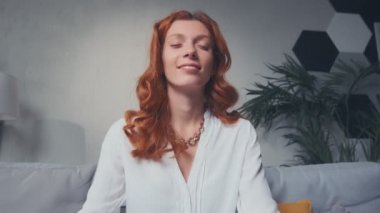 Oturma odasındaki kanepede bacak bacak üstüne atmış bir kadın meditasyon yapıyor.