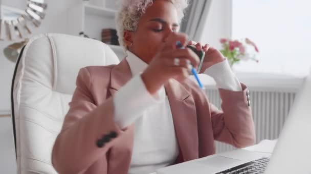 Afroamerikansk affärskvinna pratar i telefon med bärbar dator på kontoret — Stockvideo