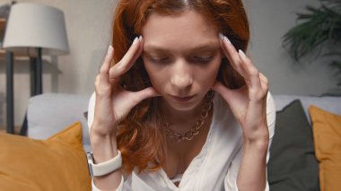 Başı ağrıyan, kızıl saçlı, üzgün genç bir kadını yakından çek..