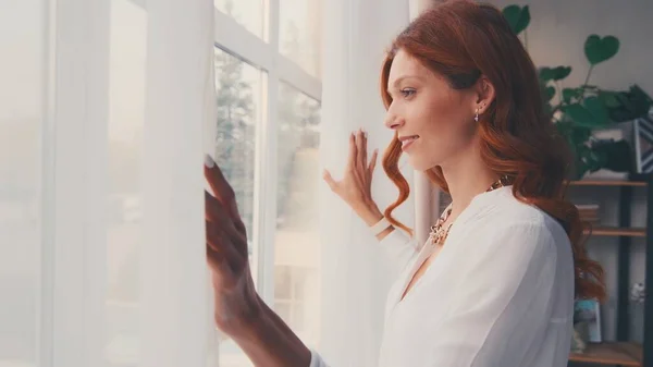 Gelukkig optimistische jonge vrouw openen gordijn kant kijken door het raam. — Stockfoto