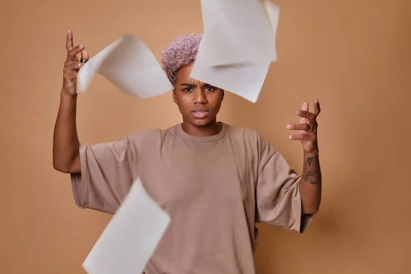 Enojado triste mujer afroamericana vomitando documentos sobre fondo beige. — Foto de Stock