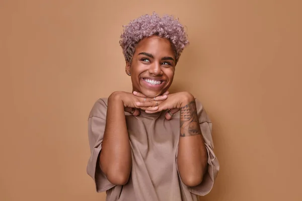 Feliz afro-americano fêmea mantém ambas as mãos sob queixo, sorri agradavelmente. — Fotografia de Stock