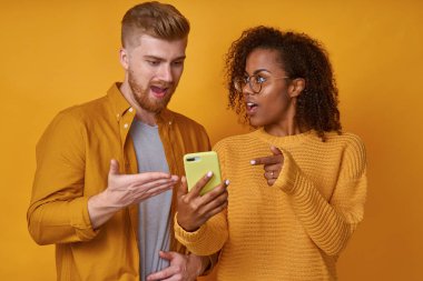 Çok ırklı Kafkasyalı erkek ve Afrikalı Amerikalı kadın telefonlarıyla ayakta duruyorlar