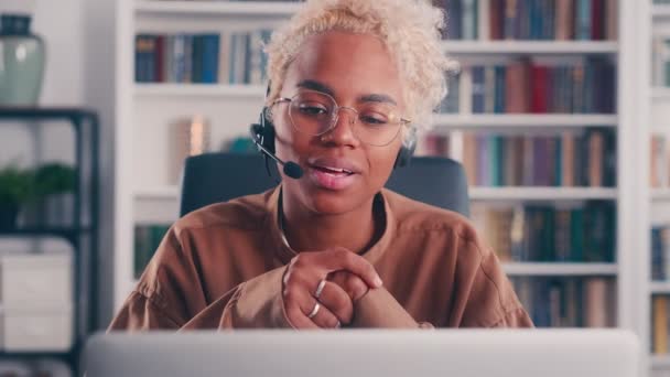 Jovem mulher de negócios afro-americana olha no laptop e usando fone de ouvido com fio — Vídeo de Stock
