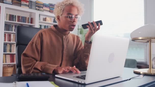 Genç Afrikalı Amerikalı girişimci telefonda konuşuyor ve dizüstü bilgisayarda yazıyor. — Stok video