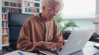 Genç Afrikalı Amerikalı kadın bilgisayar kullanarak ofis masasında oturuyor.