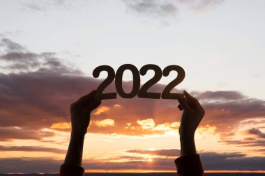 Eller 2022 numaralı ahşap parçayı günbatımının arka planında tutuyor. Ekoloji. Mutlu yıllar konsepti. kopyalama alanı. Mutlu Noeller.
