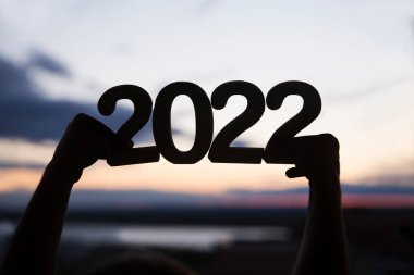 Eller 2022 numaralı ahşap parçayı günbatımının arka planında tutuyor. Ekoloji. Mutlu yıllar konsepti. kopyalama alanı. Mutlu Noeller.