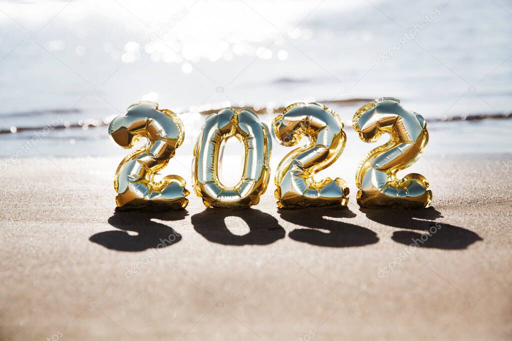 Foil balloons numeral 2022 on the sand on the beach.  happy holiday concept 