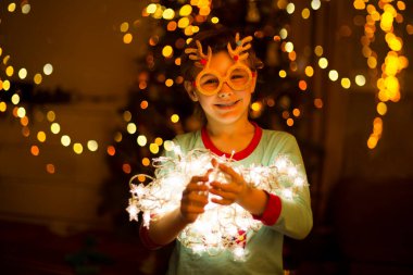 Parti gözlüklü, Noel çelenkleri parıldayan şirin bir çocuk. Evdeki ağacın yanında. 