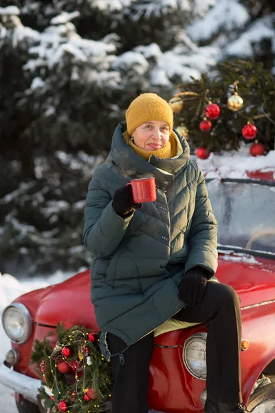 穿着温暖冬衣的老妇人站在街上喝茶 圣诞快乐 图库图片