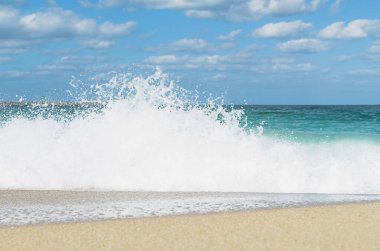 Güneşli bir günde kumlu bir sahilde köpüklü dalgalar.