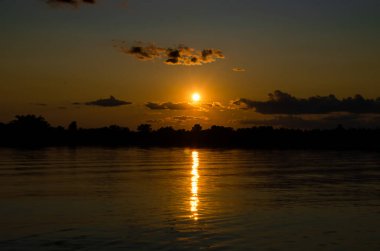 Bir gölün kıyısında gün batımı, sıcak bir yaz akşamında, suda bir yansımayla.